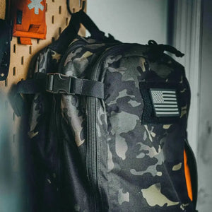 Multi-camouflage backpack with American flag patch hanging on wall.