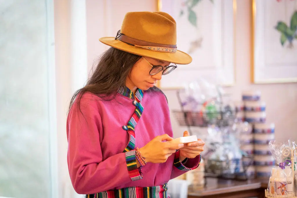 A woman in a pink traditional outfit and brown hat holds almond milk soap.