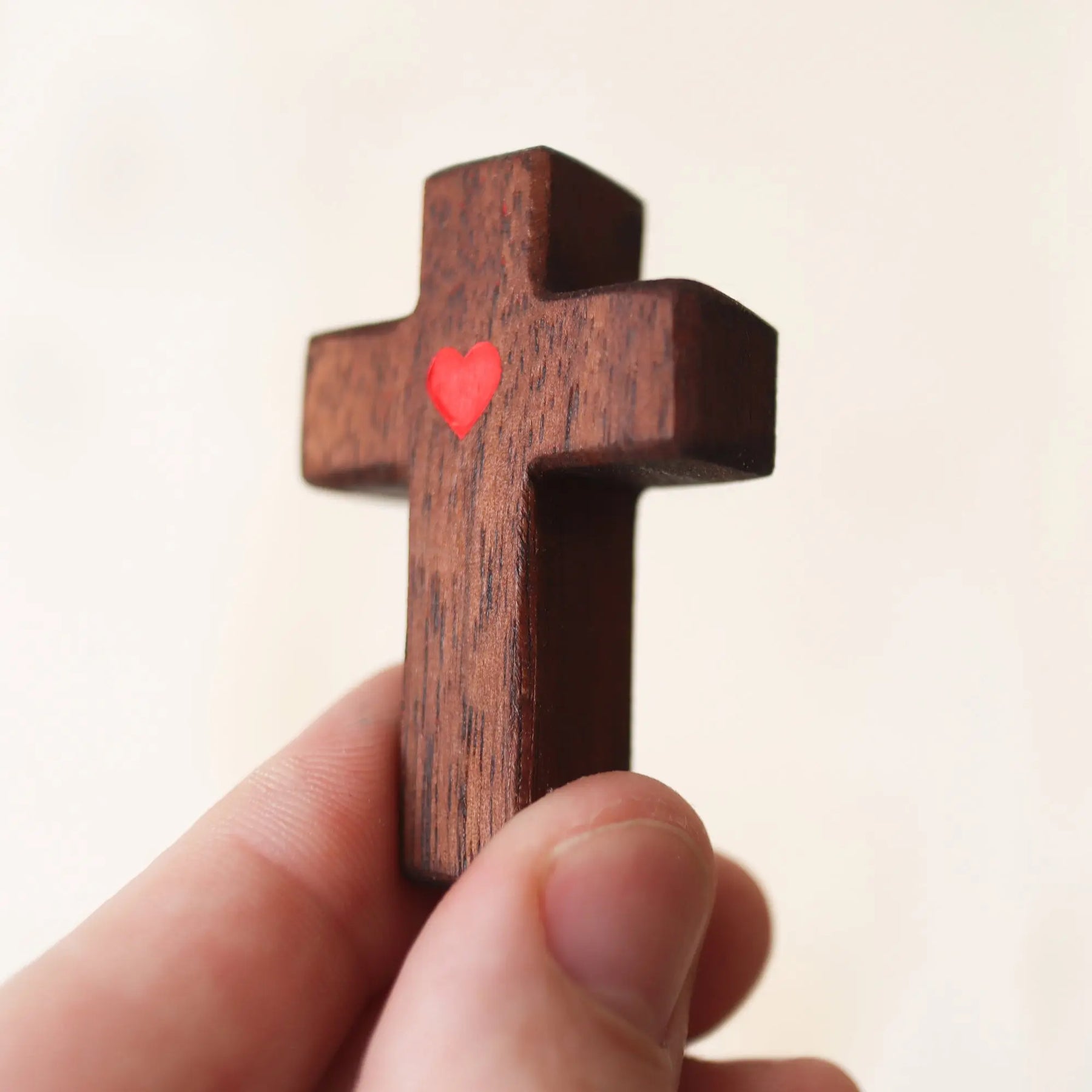 Wooden cross with a small red heart detail held in a hand.
