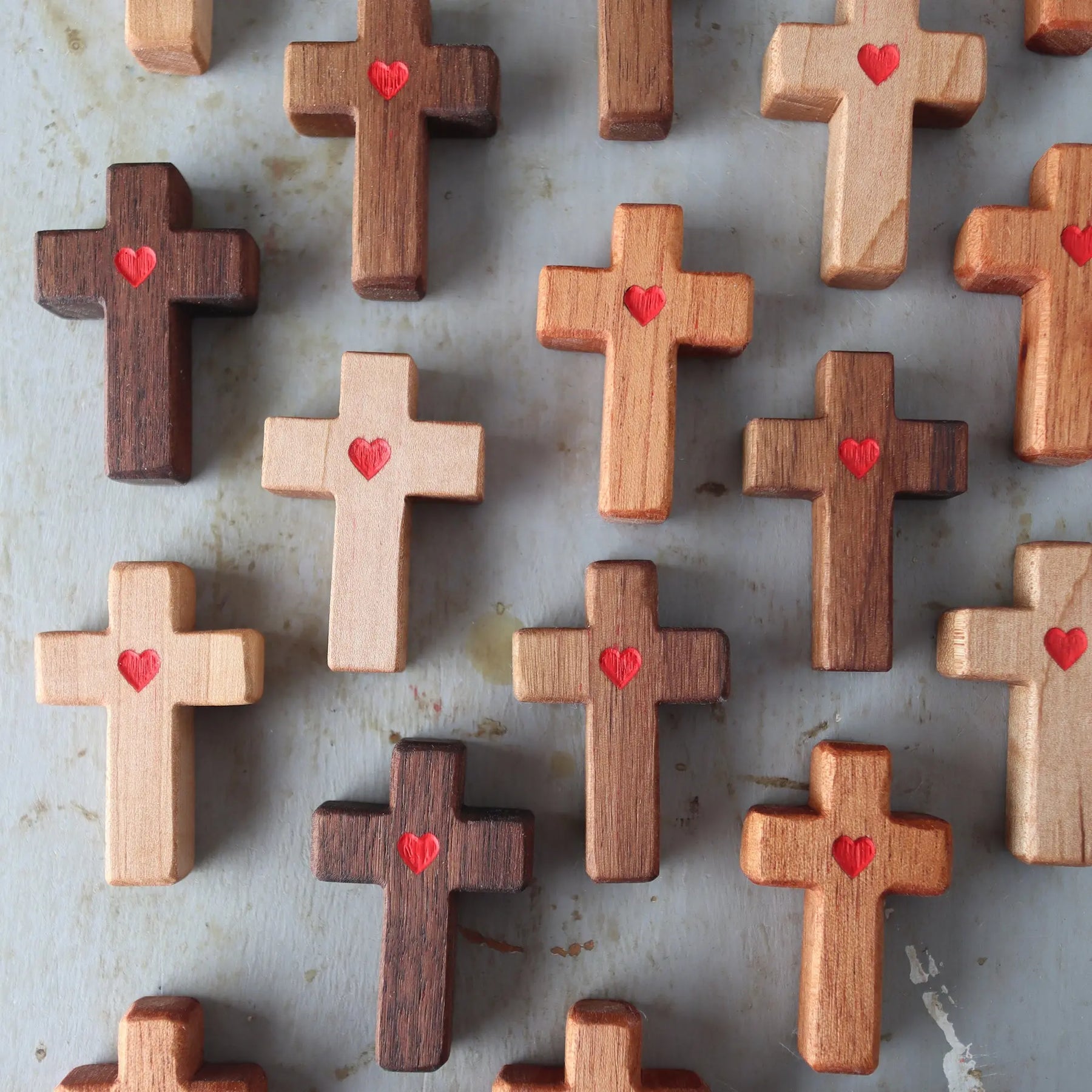 Wooden crosses with carved red hearts arranged on a surface.