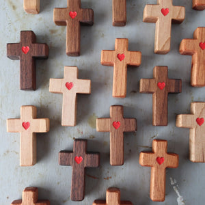 Wooden crosses with carved red hearts arranged on a surface.