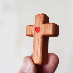 Wooden cross with a red heart design held in a hand.