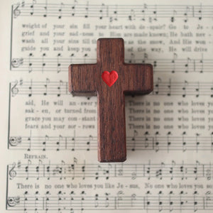 Wooden cross with a red heart rests on sheet music.