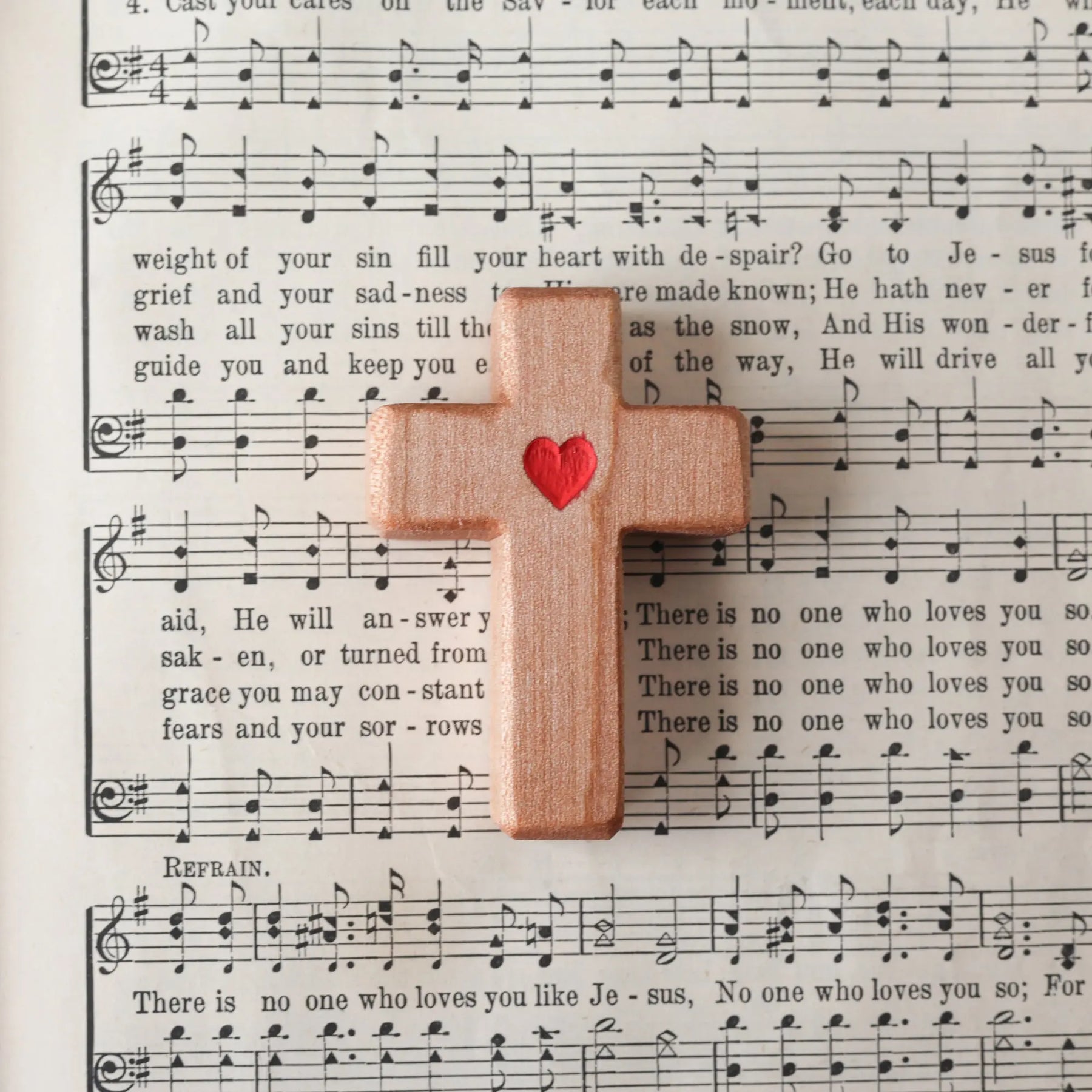 Wooden cross with a red heart placed on a page of sheet music.