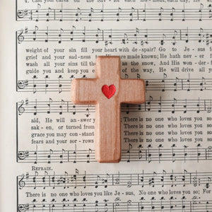 Wooden cross with a red heart placed on a page of sheet music.