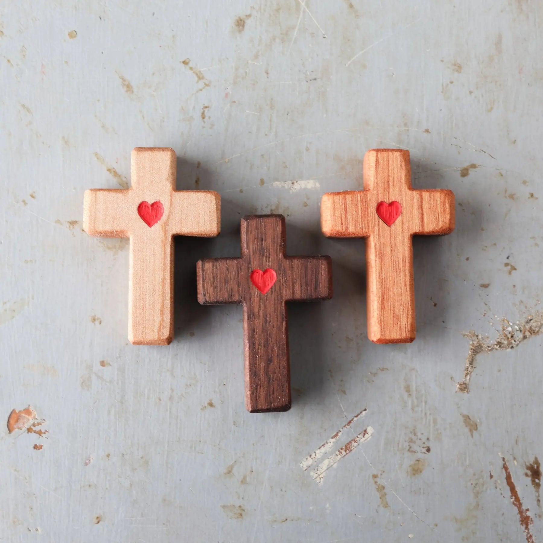 Three wooden crosses with carved red hearts on a distressed surface.
