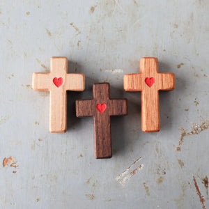 Three wooden crosses with carved red hearts on a distressed surface.