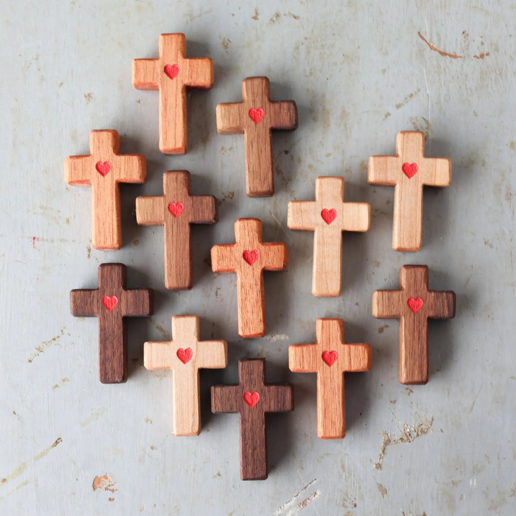 Wooden crosses with carved red hearts arranged on a textured surface.