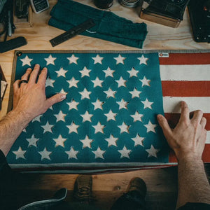 Hands touching a large American flag made from recycled fire hose, showing stars and stripes.