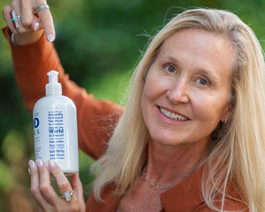 Woman holding white bottle of Arni•cover•y Arnica + Mint Lotion with text on label.