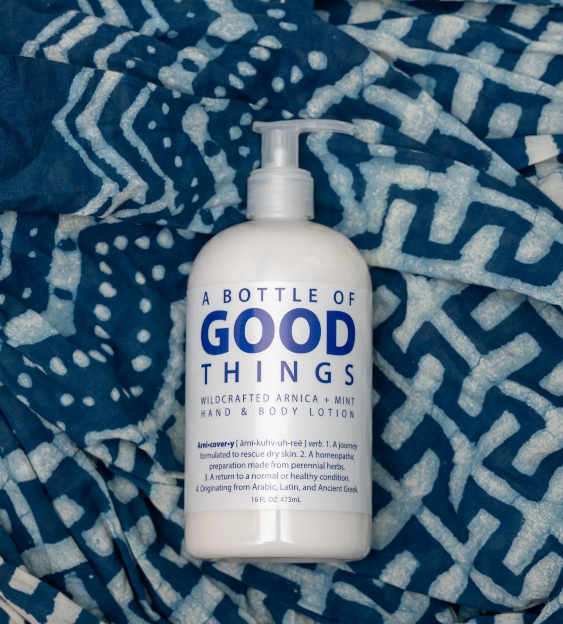 White pump lotion bottle with blue text, 'Arnica Mint Hand & Body Lotion', on blue patterned cloth.