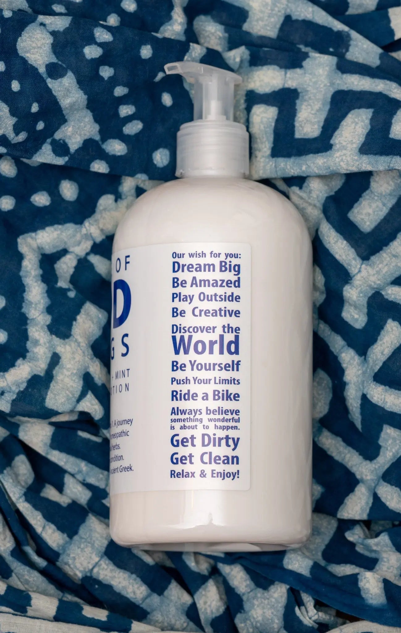 White pump bottle of Arnica Mint Hand and Body Lotion on blue patterned fabric.