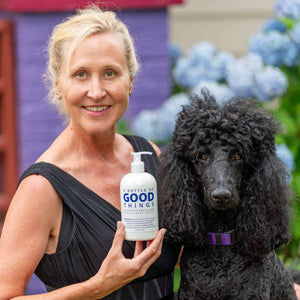 Woman holding a bottle of Good Things Arnica + Mint Hand & Body Lotion next to a black poodle.