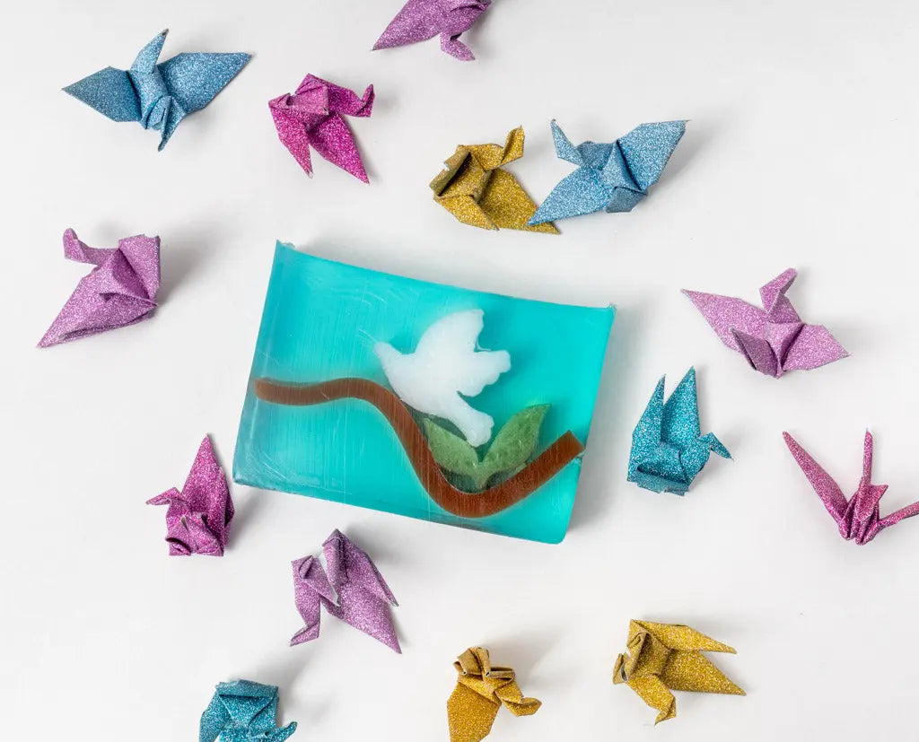 Blue soap slice with white bird on branch, surrounded by colorful origami cranes.