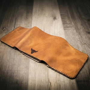 Brown leather trifold wallet with a bull emblem on a wooden surface.