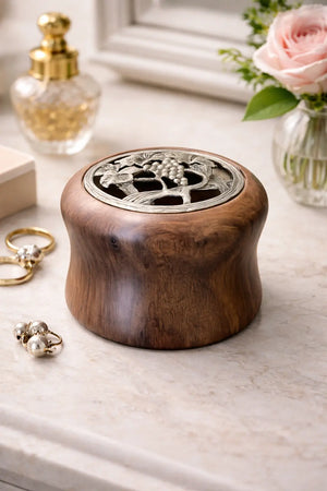 Walnut treasure box with decorative metal lid featuring a grapevine design, placed on a marble surface with jewelry and perfume.