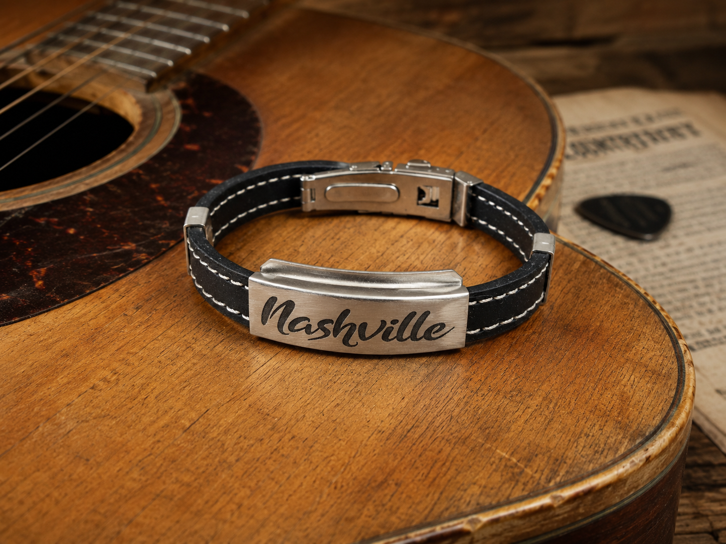 Black and silver bracelet with 'Nashville' engraving on a wooden surface with an acoustic guitar.