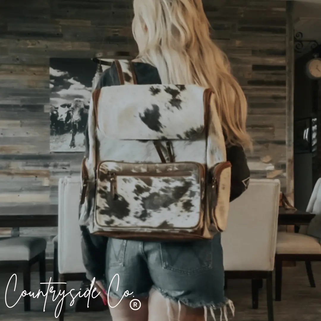 Cowhide backpack with brown leather trim and a black and white spotted pattern.