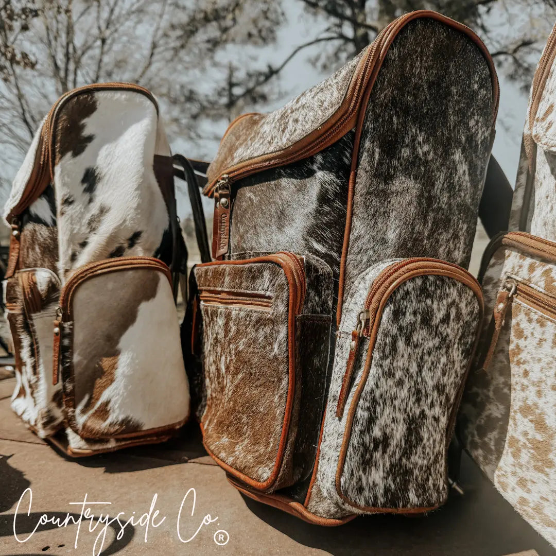 Brown and white cowhide backpack with leather trim and multiple zippered pockets.