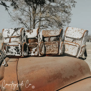 Four cowhide conceal carry backpacks with leather accents on a vintage truck.