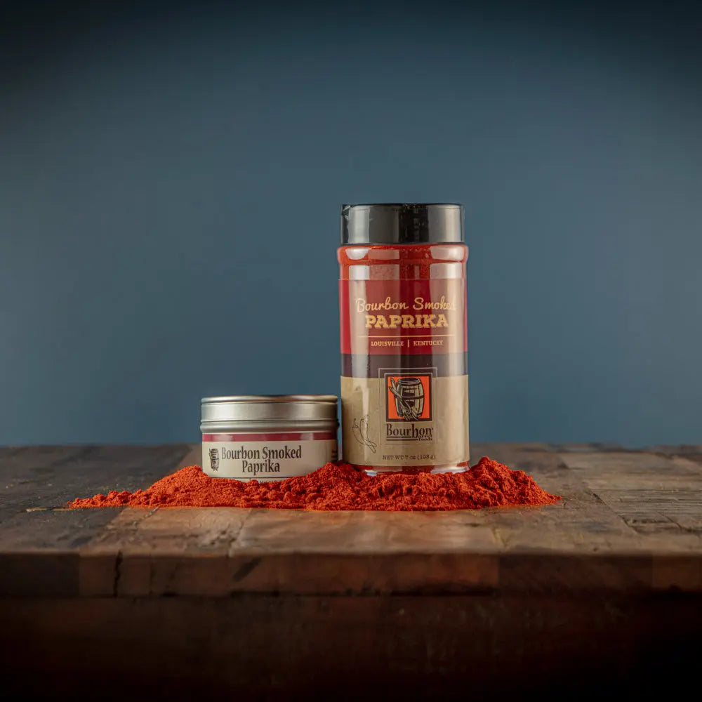 Bourbon Smoked Paprika in a tin and bottle with spilled paprika on wood.