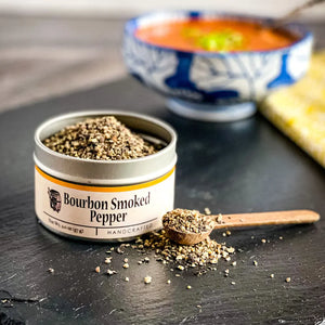 Bourbon Smoked Pepper in a tin with a wooden spoon on a dark surface