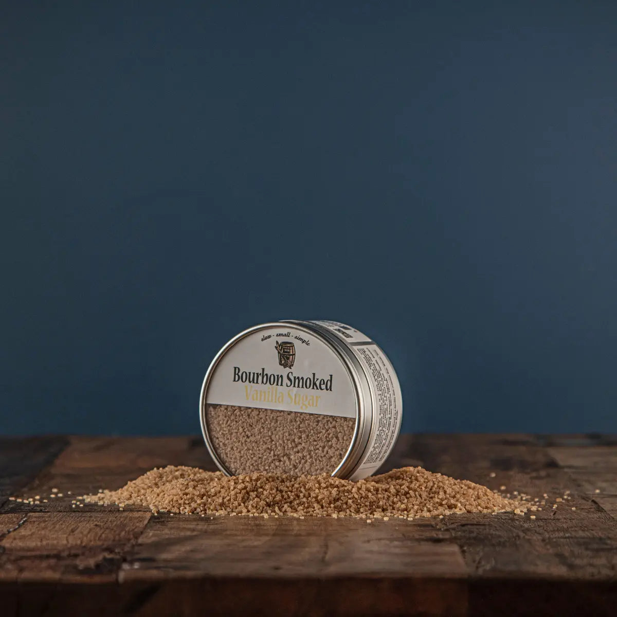 Bourbon smoked vanilla sugar in tin with scattered sugar on wood