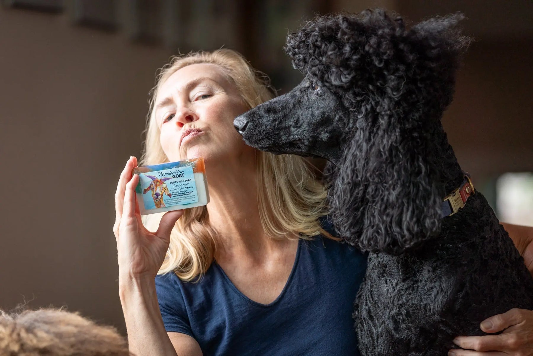 Woman holding Coconut Lime Verbena goat milk soap bar with a black poodle dog