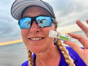 Woman holding coconut milk lip butter tube with Appalachian Goat branding on a beach