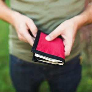 Red and black wallet made of fire hose material held by hands.