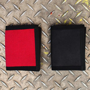 Two bi-fold wallets, one red canvas and one black, on a textured metal surface.