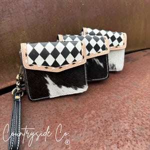 Three black and white cowhide wallets with checkered flaps and wristlet straps.
