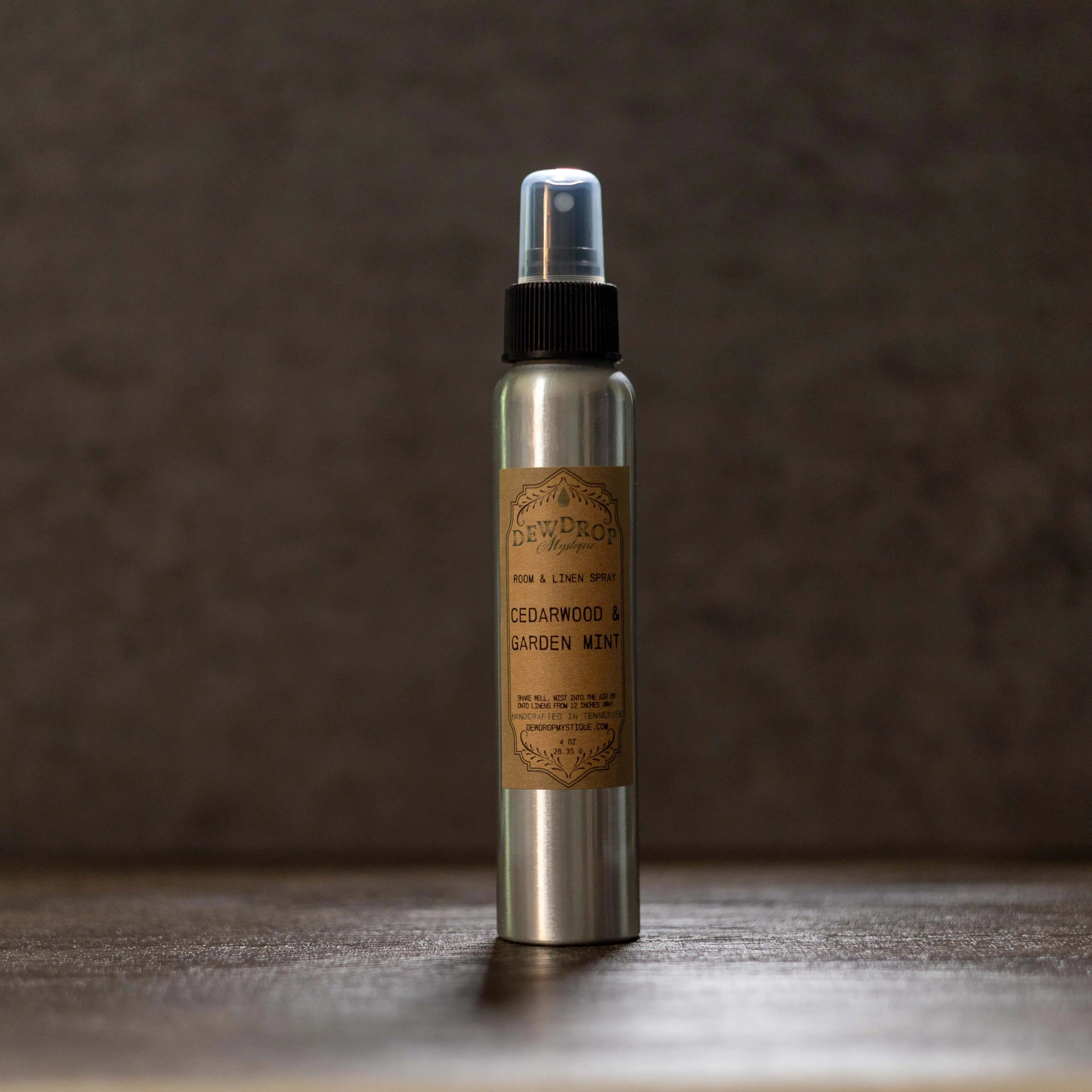 Cedarwood & Garden Mint Room Spray in a silver bottle with black spray nozzle and a brown label on a brown surface