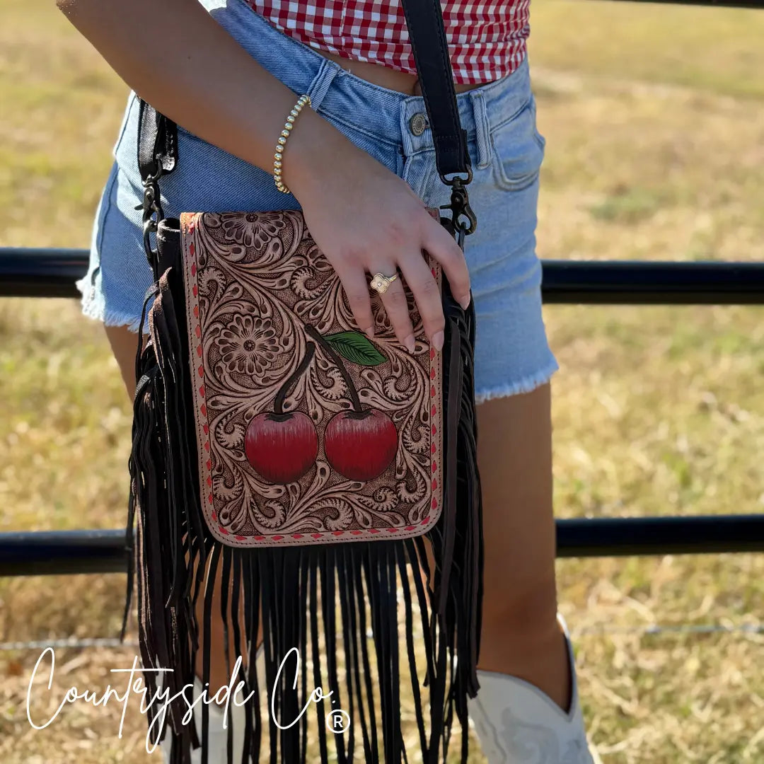 Brown tooled leather crossbody purse with red cherries and fringe.