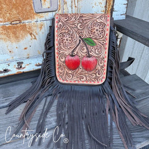 Tooled leather crossbody purse with red cherries and dark fringe.
