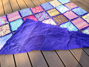 Colorful patchwork rag quilt with purple fleece backing on a wood deck.