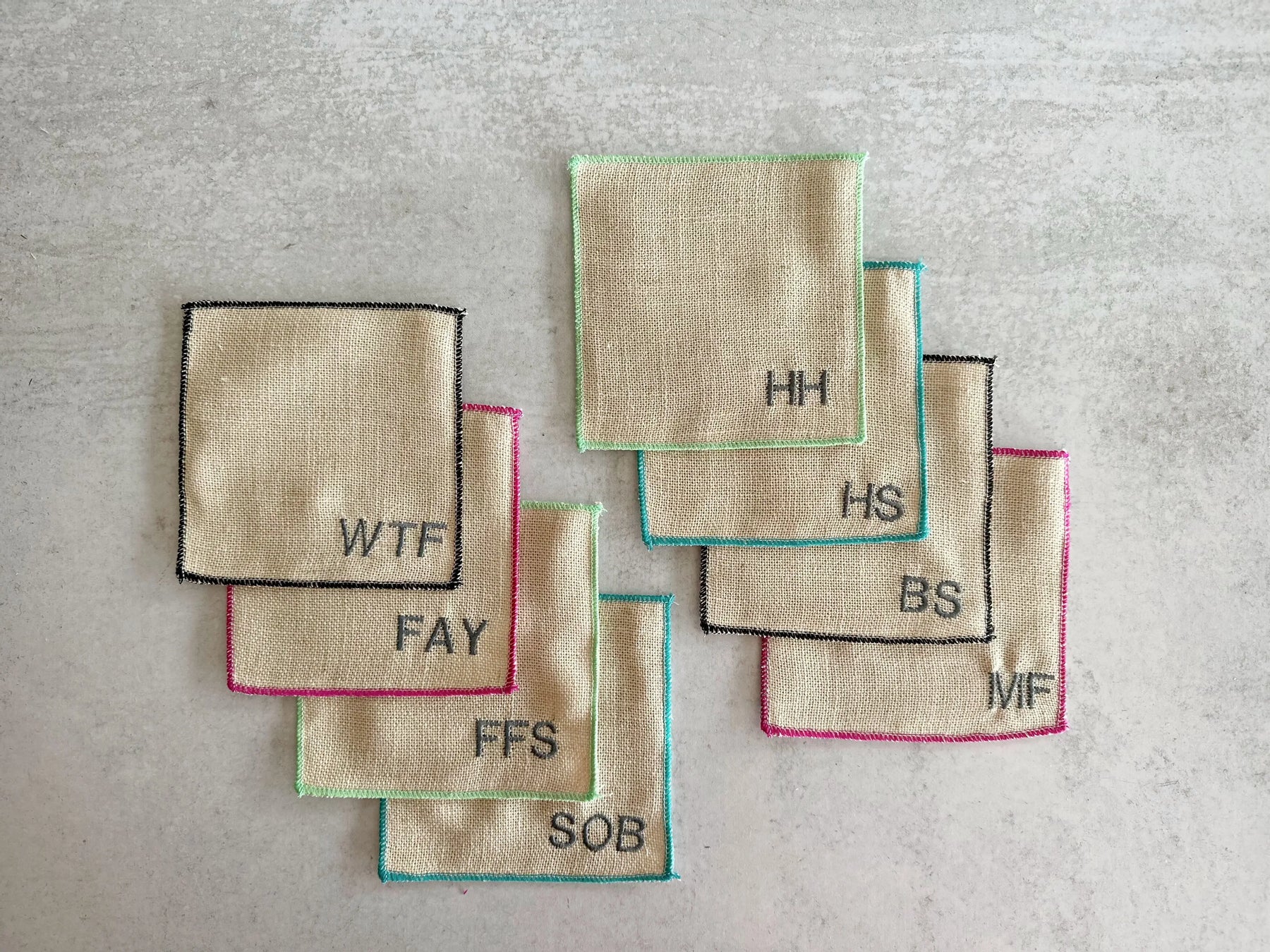 Set of 8 sweary cocktail coasters with embroidered letters and colorful edges.