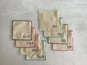 Set of 8 sweary cocktail coasters with embroidered letters and colorful edges.
