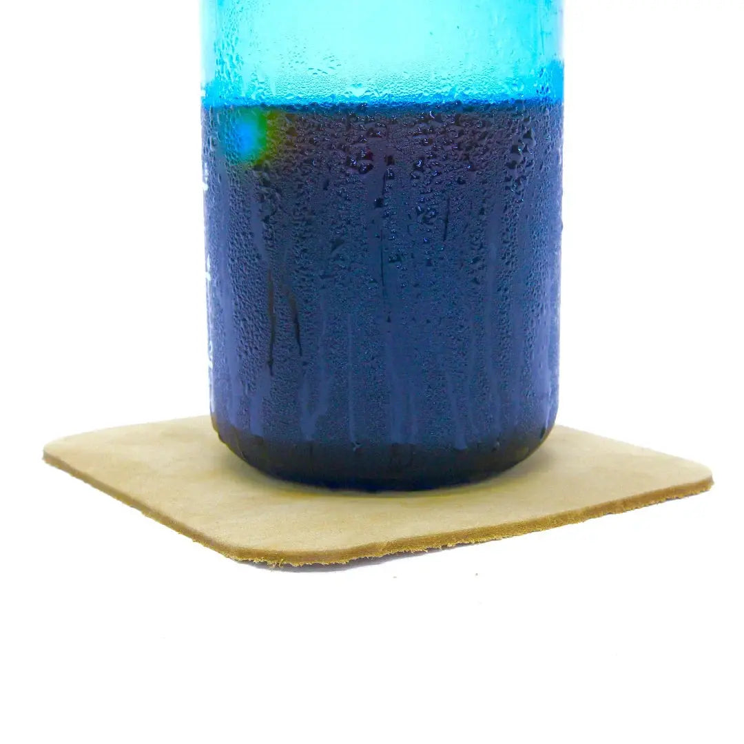 Blue drink in a glass on a tan leather coaster.