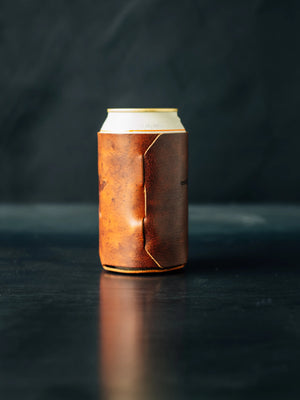 Cognac leather coozie on dark surface holds beverage can, by Main Street Collective.