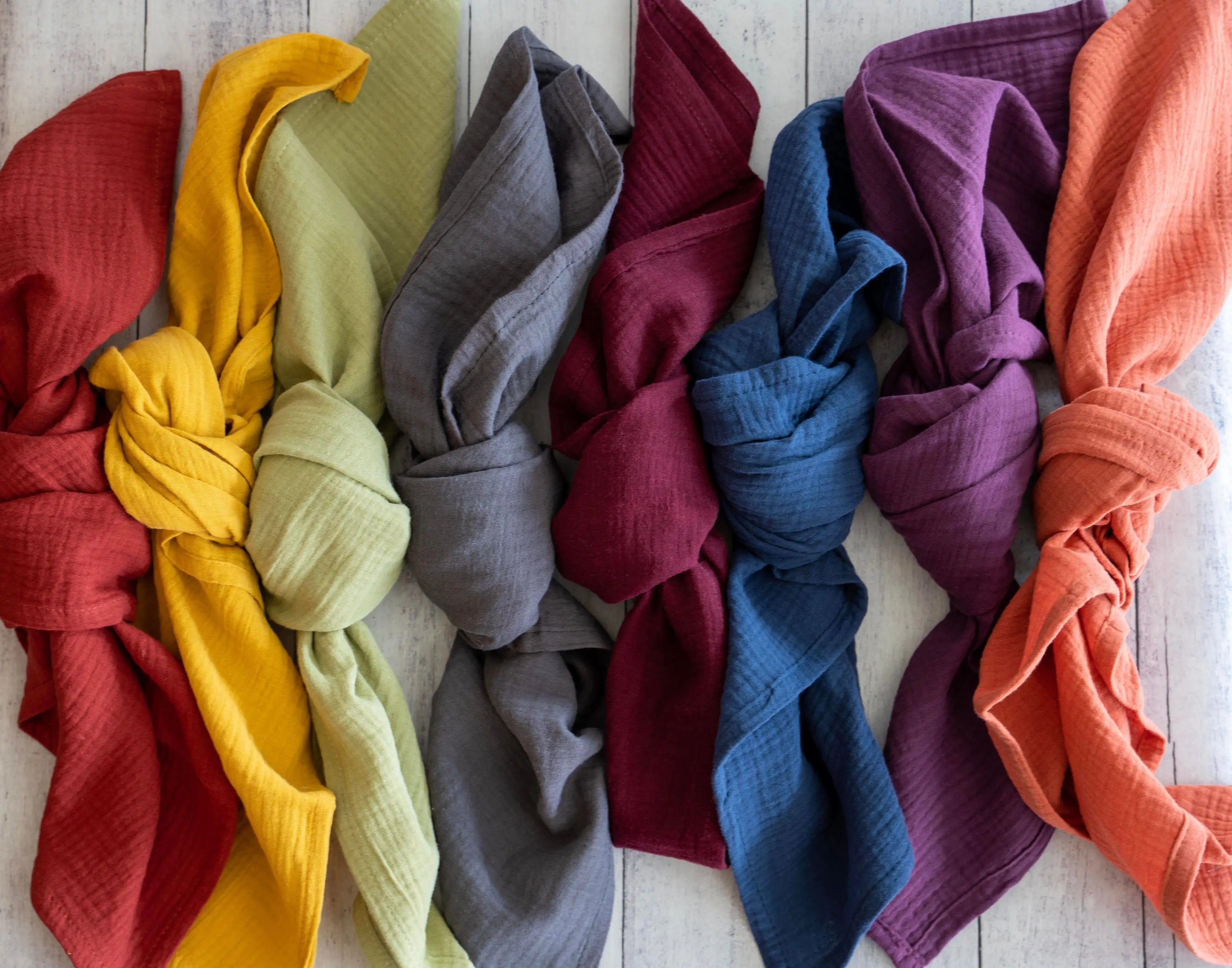 Set of four colorful crinkle cotton cloth napkins folded and arranged on a white wooden background.