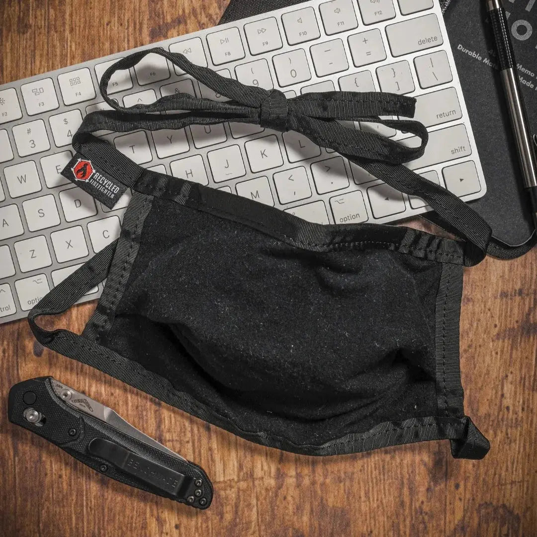 Black cotton face mask with ties on a keyboard next to a knife.