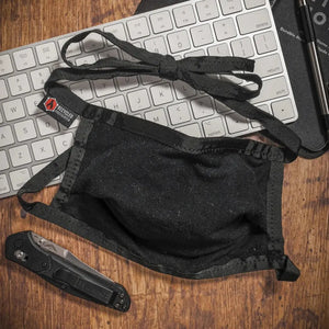 Black cotton face mask with ties on a keyboard next to a knife.