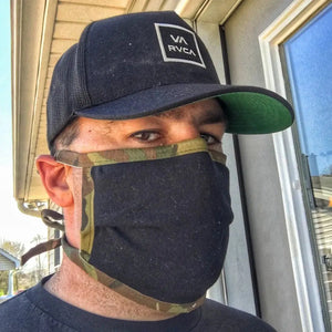 Man wearing a black cotton face mask with camouflage trim and a black baseball cap.
