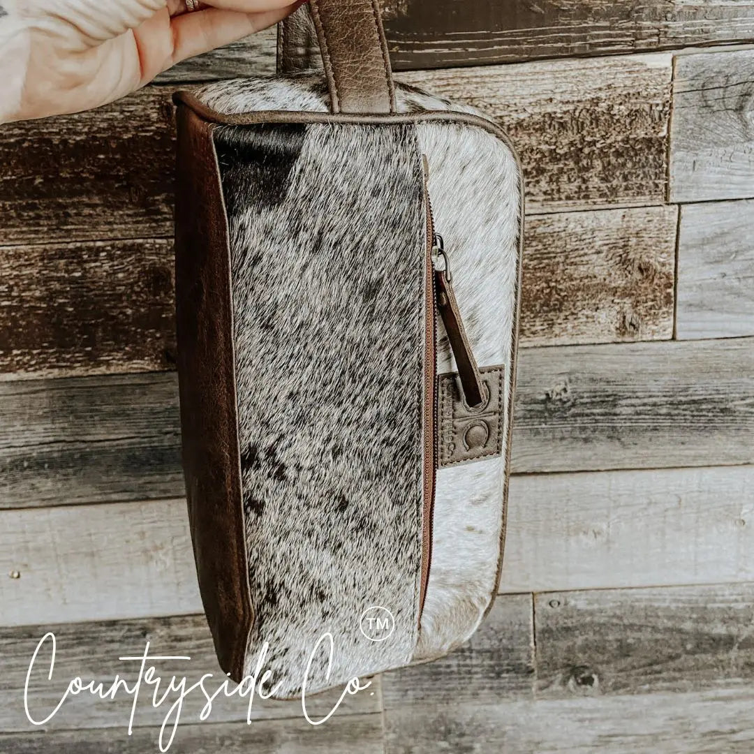 Brown leather and cowhide toiletry bag with zipper closure.