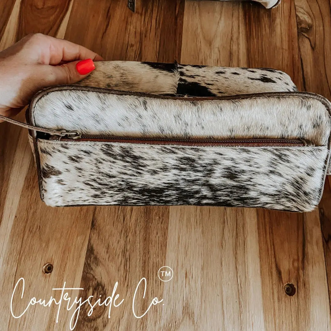 Countryside Co. cowhide toiletry bag with zipper closure on wooden background.