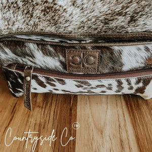 Brown and white cowhide toiletry bag with leather trim and zipper.