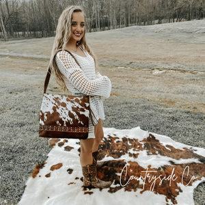 Woman wearing white crochet top and boots with a cowhide leather purse.