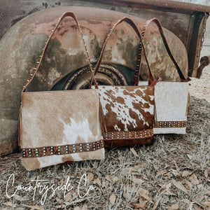 Three cowhide leather purses with braided straps and brass accents in various cow print patterns.