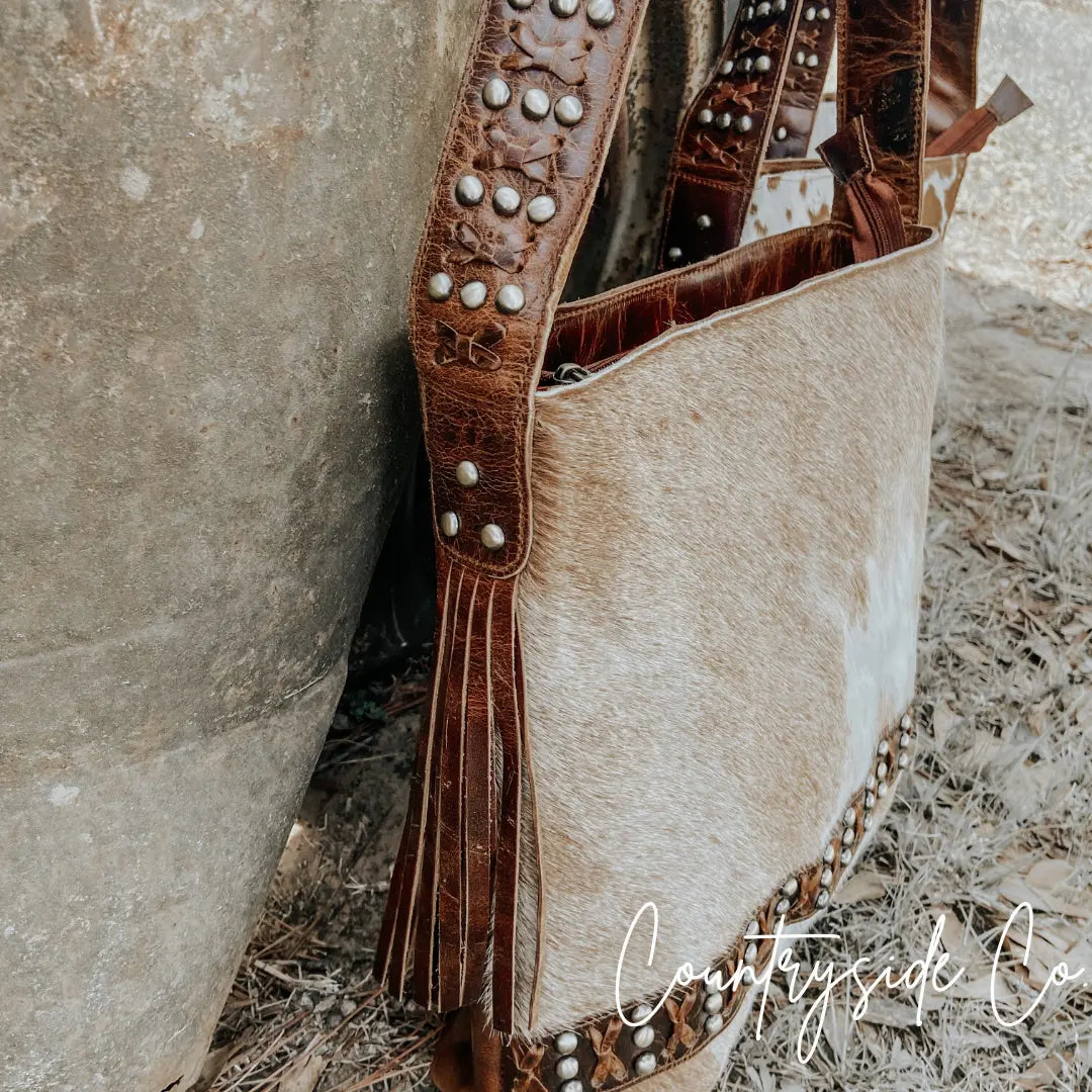 Western style cowhide leather purse with brass accents and fringe.